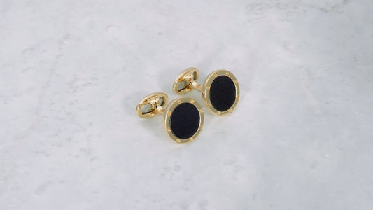 180 degree video of Onyx Gemstone with Rivet Etch Detail 18K Yellow Gold Cufflinks on a marble background. 