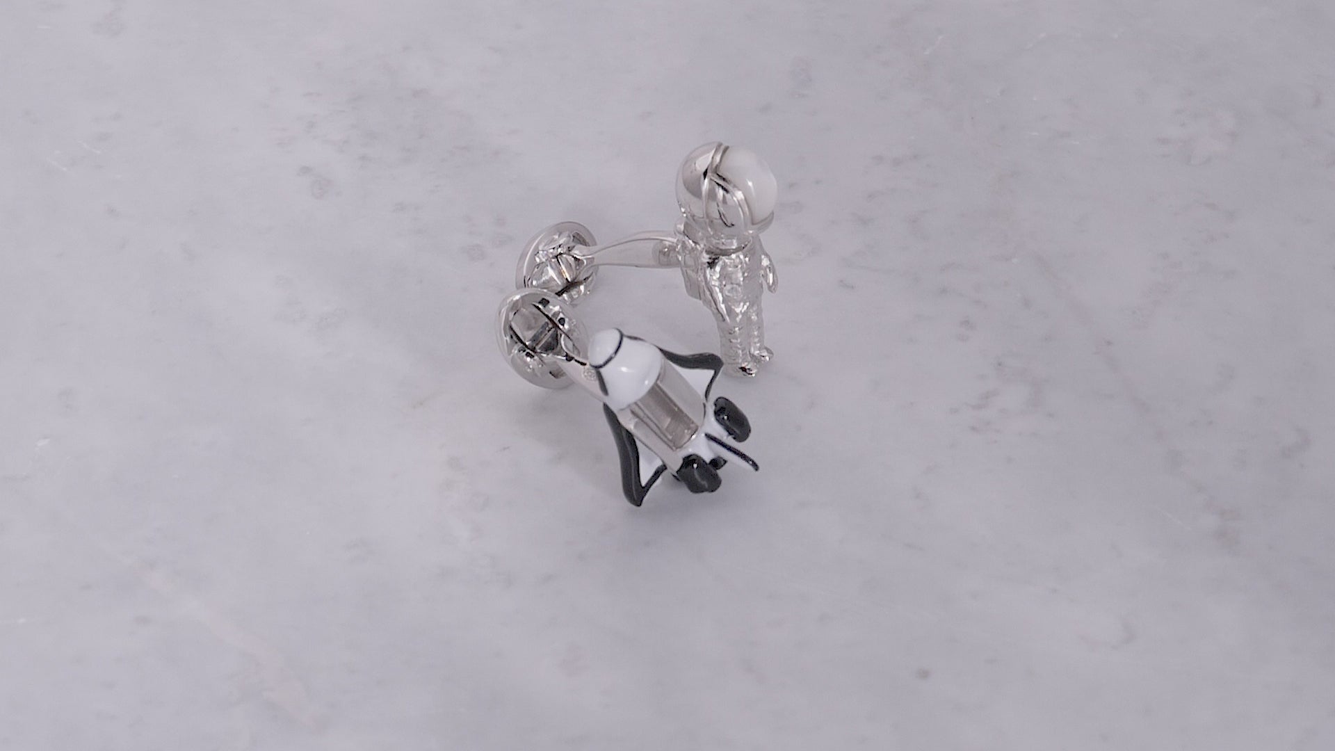 180 degree video of Jan Leslie's Shuttle & Astronaut Bobble Head Sterling Silver & Gemstone Cufflinks with open shuttle door on a marble background. 