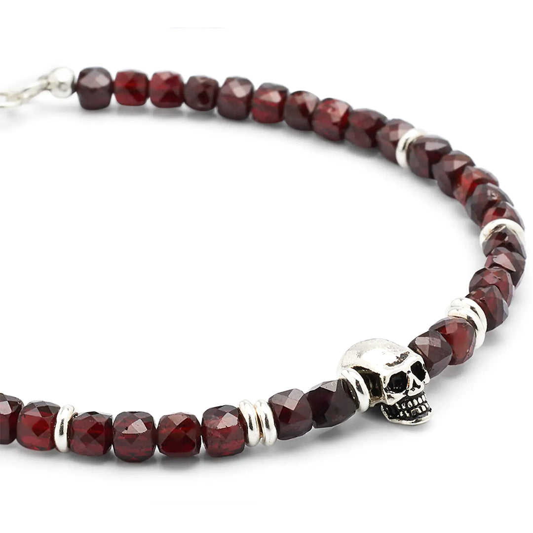 Close up of faceted garnet gemstones, sterling silver skull, and sterling silver spacer beads on the Faceted Garnet Gemstone Beaded Bracelet with Sterling Silver Skull Media. 