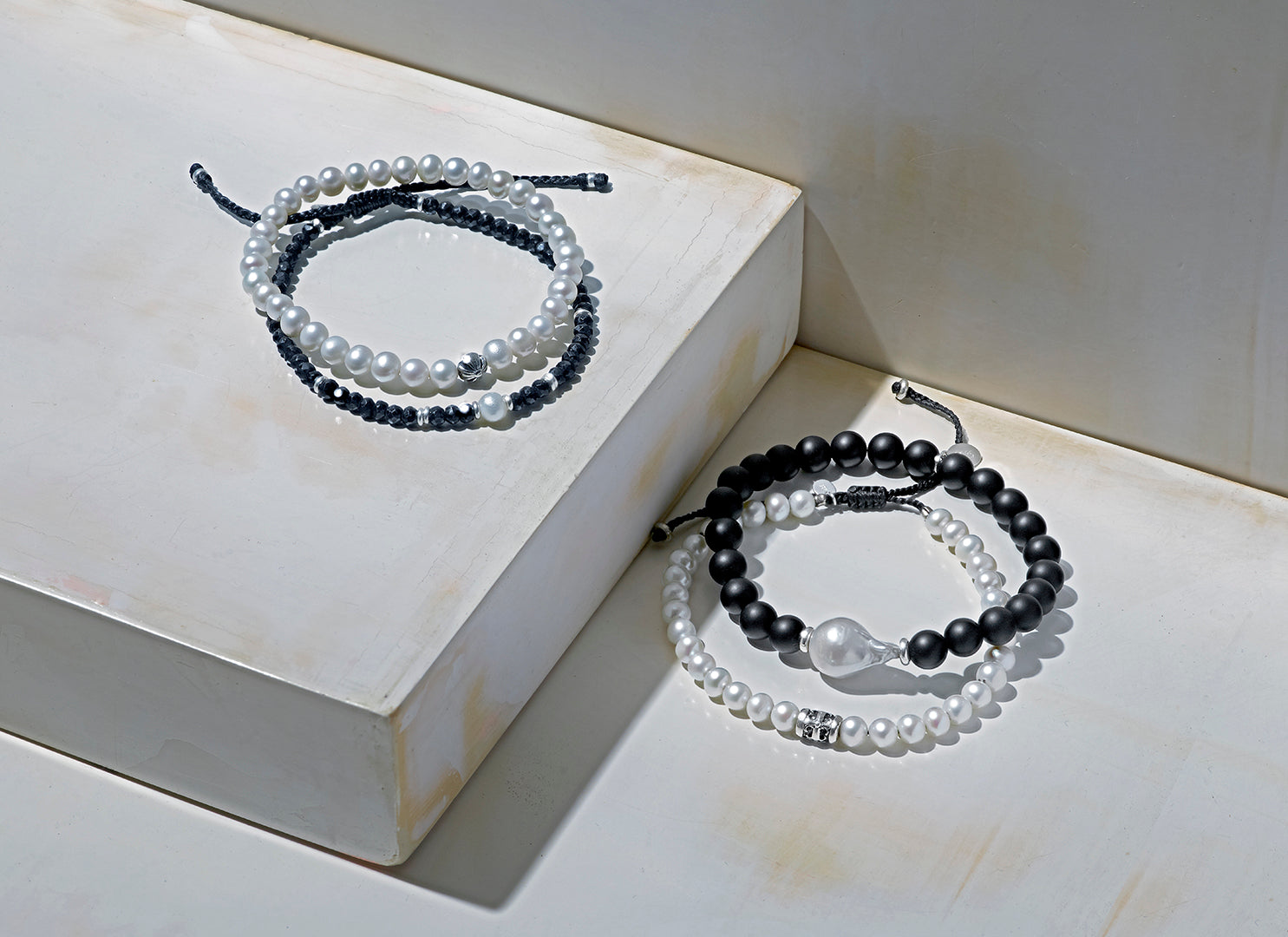 Group shot of Jan Leslie's Luxe Pearl Collection bracelets on risers. From left to right: Men's Freshwater Pearl Stretch Bracelet with Sterling Silver Fluted Star Spacer, Men's black onyx bracelet with freshwater pearl center, Men's freshwater pearl bracelet with filigree spacer. 