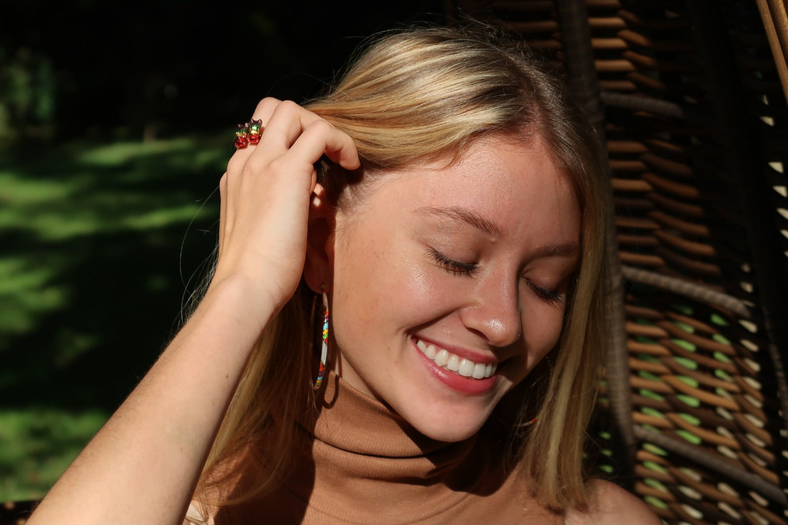 Smiling female model wearing Jan Leslie's SINGLE Rainbow Gummy Bear Sterling Silver Ring with 18K Gold Vermeil, and Stripe Enamel & Gemstone Sterling Silver 55MM Hoop Earrings in rainbow on gold. 