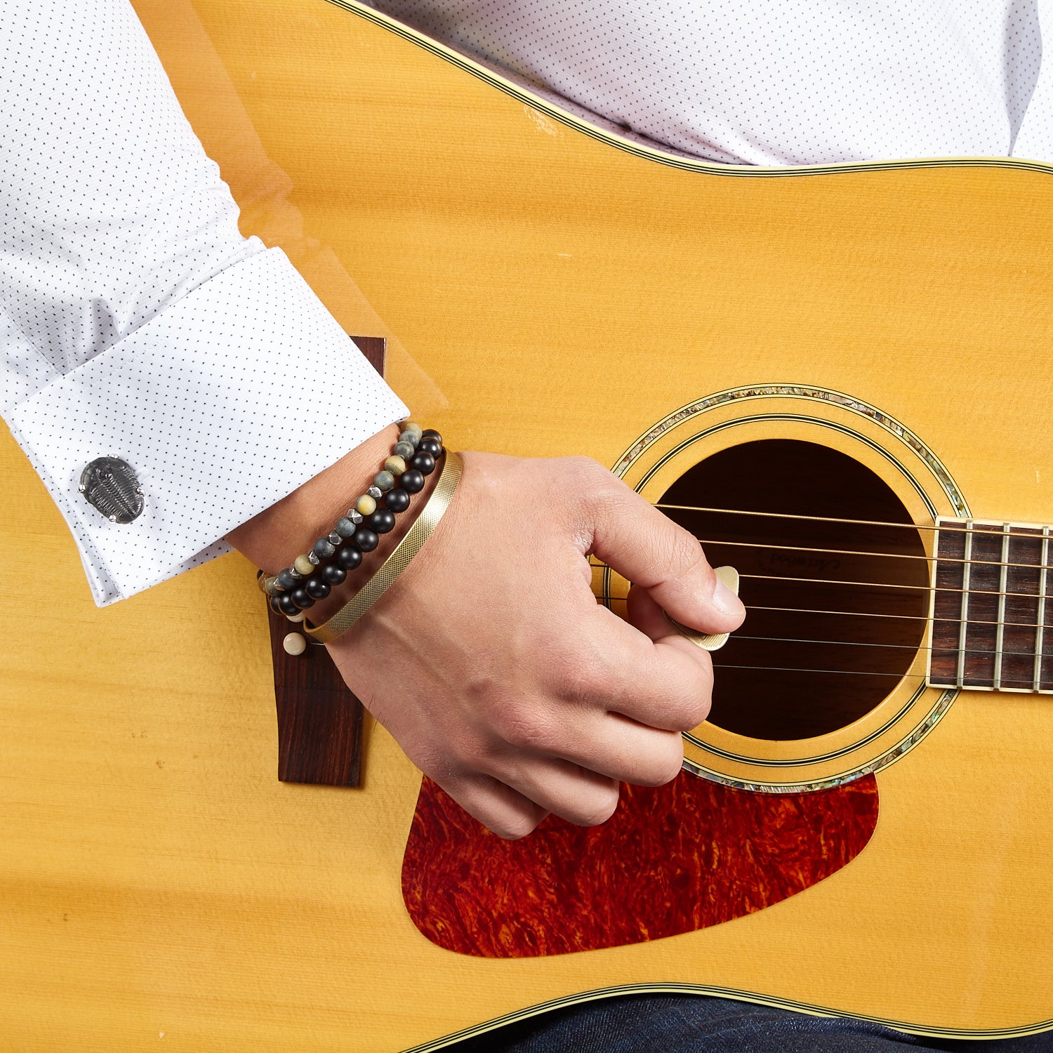 Close up of male models wrist donning Delta Trilobite Fossil Sterling Silver Cufflinks on a patterned white cuffed shirt. 