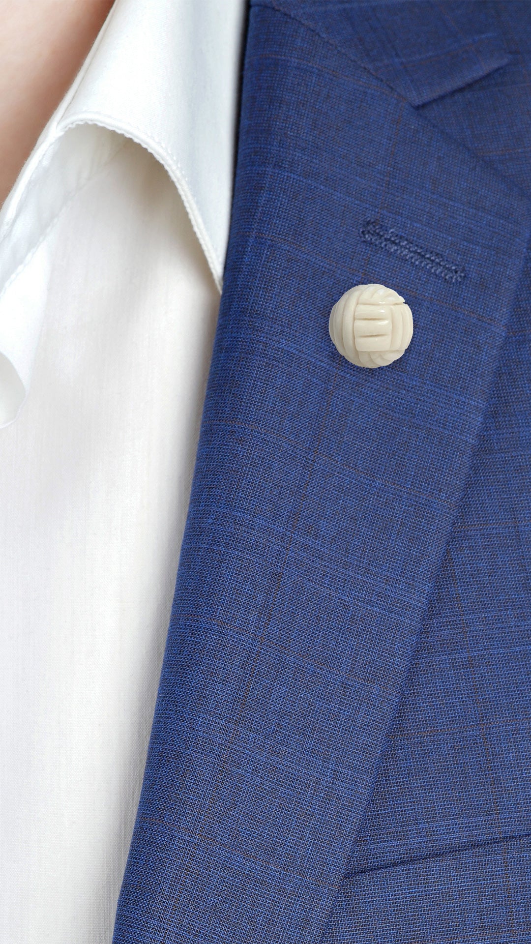 Male model wearing Hand-Carved Mystical Knot Gemstone Sterling Silver Lapel Pin in bone on a navy blue suit jacket. 