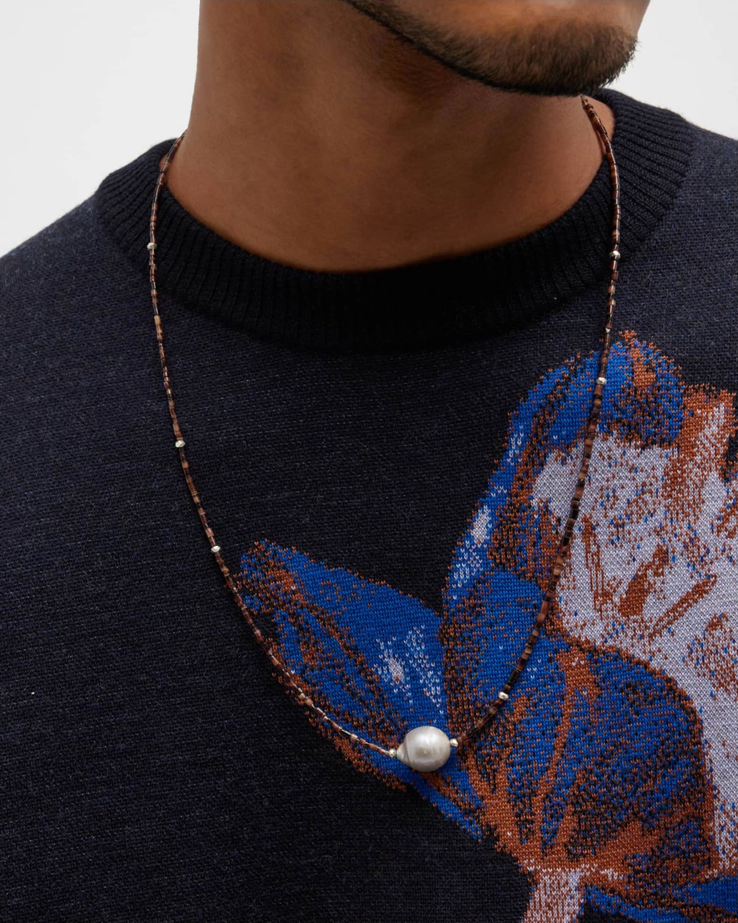 Close up of a male models neck wearing the Freshwater Pearl Center Chocolate Shell Beaded Necklace with Sterling Silver Accents. 