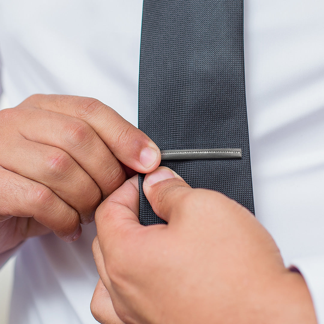 Close up of male model putting on Gunmetal Sterling Silver Tie Bar with CZ stones on a dark grey tie. 