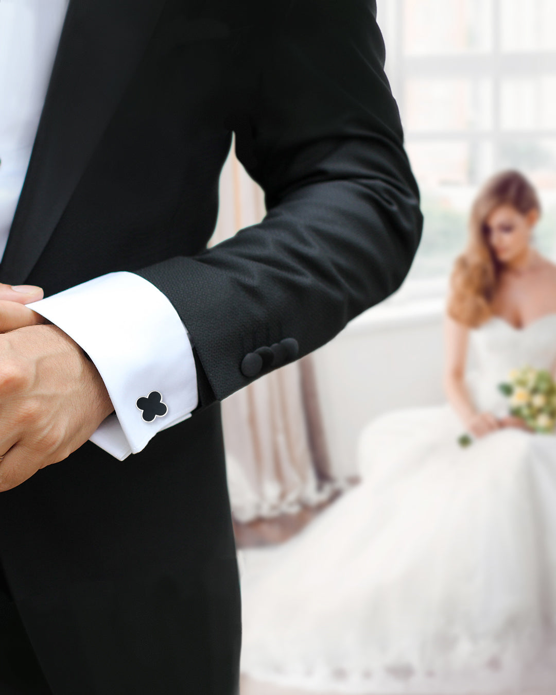 Photo of close up of male modes wrist and arm wearing the Four Leaf Clover Gemstone and Sterling Silver Cufflinks with onyx inlay on a white cuffed shirt and black tuxedo with sitting bride in the background. 